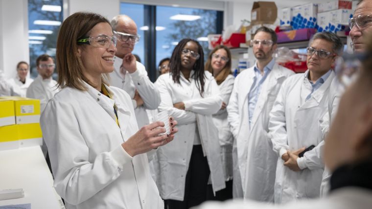 Group of people in lab coats listening to presenter in lab