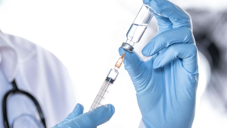Gloved hands holding a vaccine vial